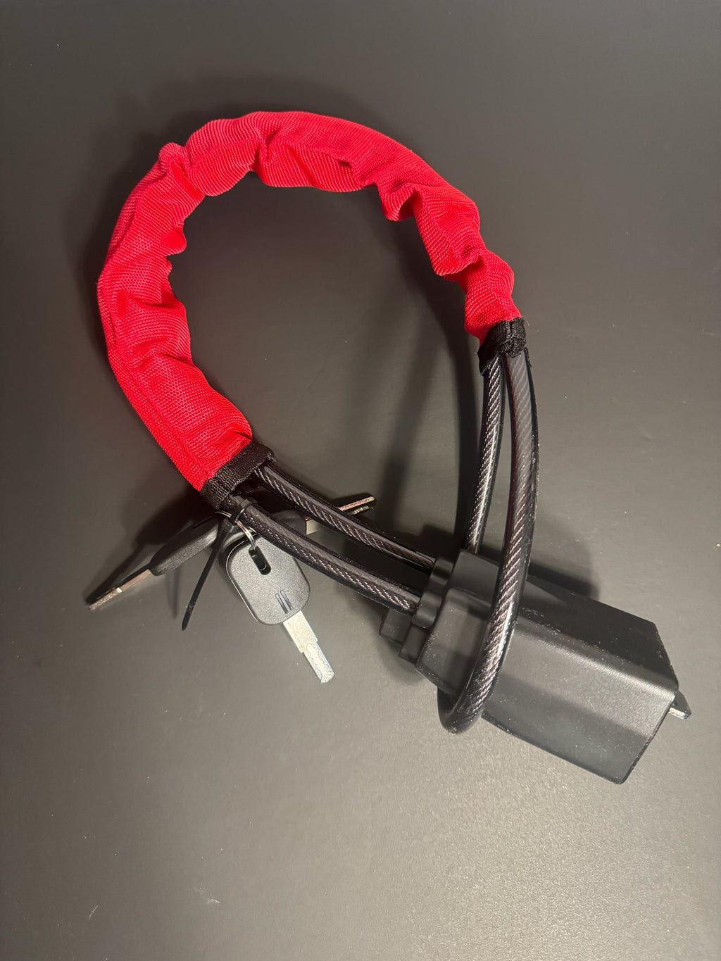 KMD MarketHub red fabric-covered steel cable steering wheel anti-theft lock with keys on a dark surface
